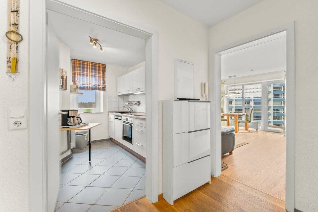 Een moderne keuken met witte kasten, een eethoek met een tafel en stoelen, en een uitzicht op een gebouw door grote ramen.