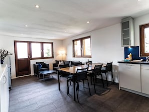 Eine moderne Küche mit Essbereich, ausgestattet mit einem Holztisch, schwarzen Stühlen und einem eingebauten Backofen.