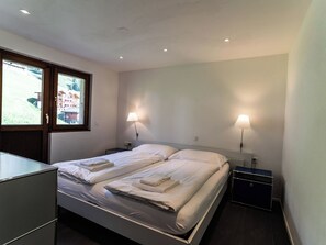 A hotel room with a bed, two bedside tables, a desk, and a window with a view of buildings. - Sportina 33 3. OG Süd-West Appartement/Fewo, Dusche und Bad, WC by Interhome (Riederalp)