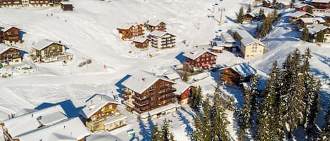 A snow-covered mountain village with wooden buildings, ski slopes, and ski lifts.