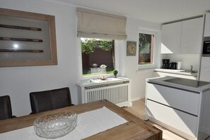 A modern kitchen with white cabinets, a built-in oven, and a window with a view of greenery. - Holiday apartment with 1 bedroom (St. Peter-Ording)