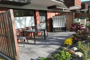 Eine Terrasse mit Tisch und Stühlen, einem Grill und einem Garten mit verschiedenen Pflanzen.