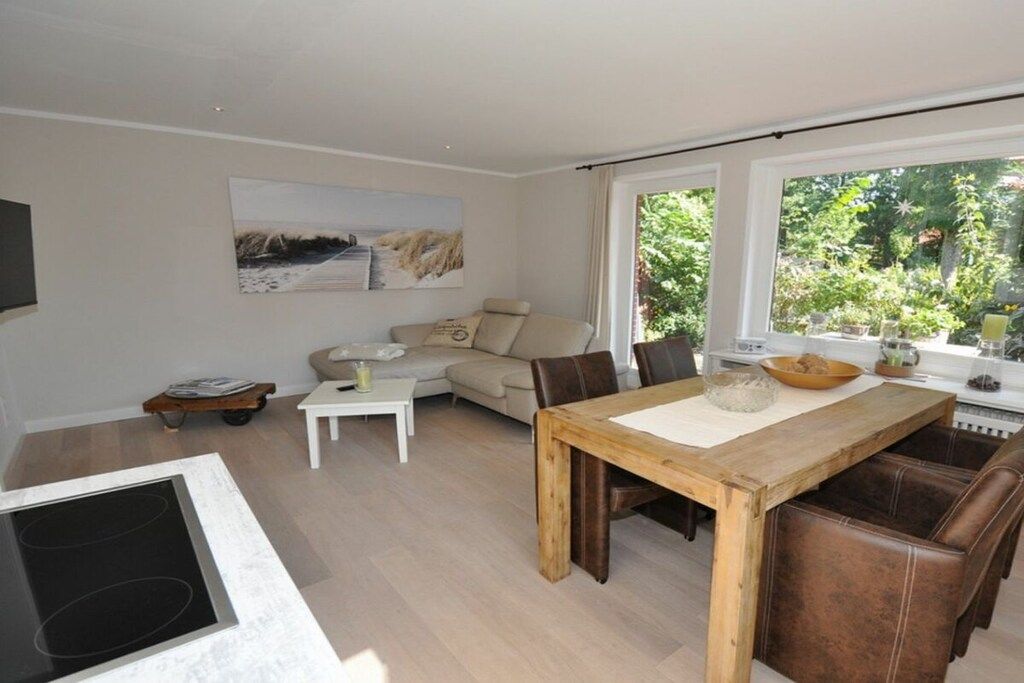 A modern living room with a dining area, a sofa, a coffee table, and a large window with a view of greenery.