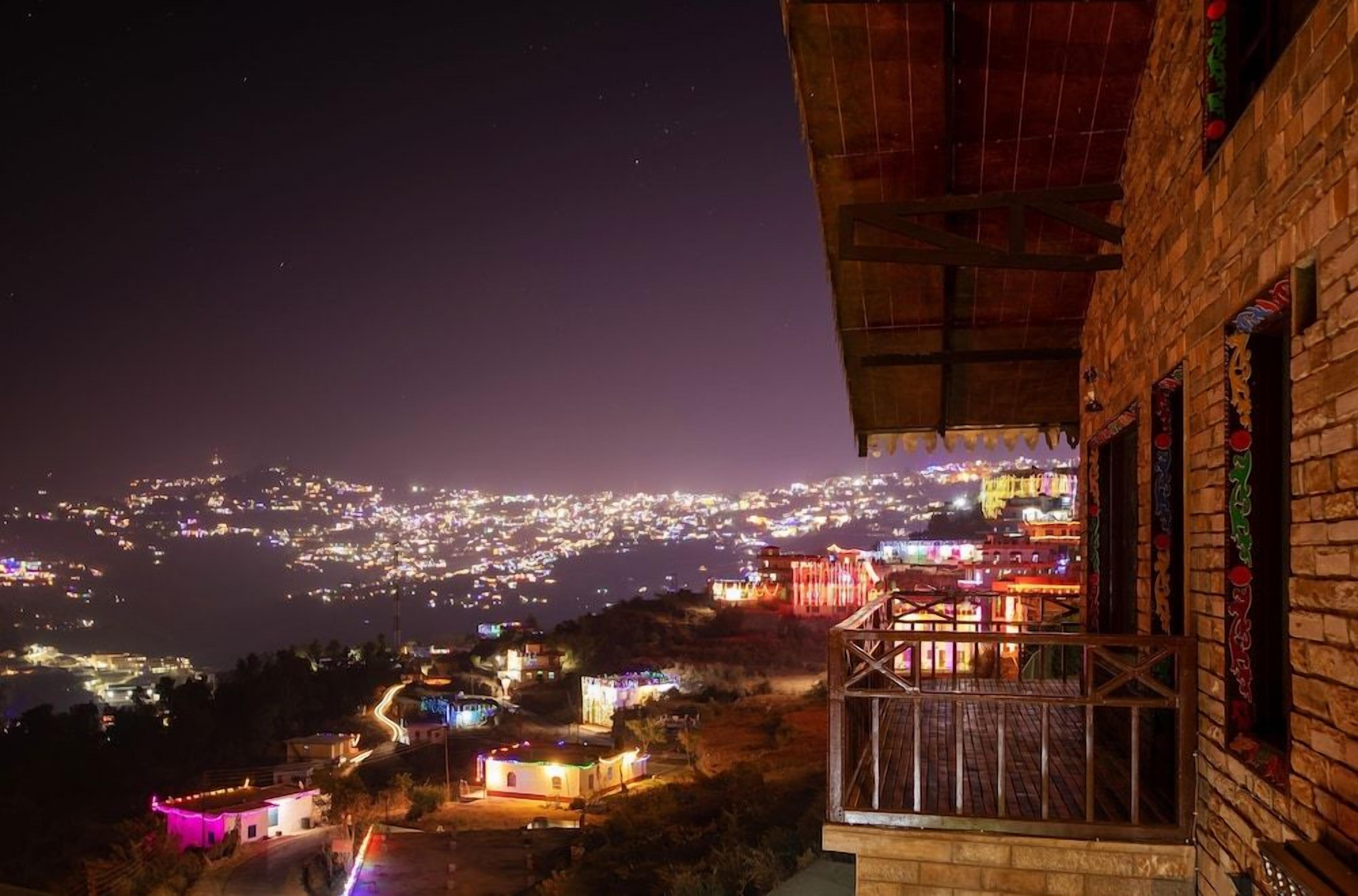 A night view of a city with illuminated buildings and a balcony overlooking the scene.