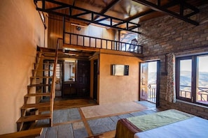 Um quarto amplo com mezanino, escada de madeira e uma grande janela com vista.