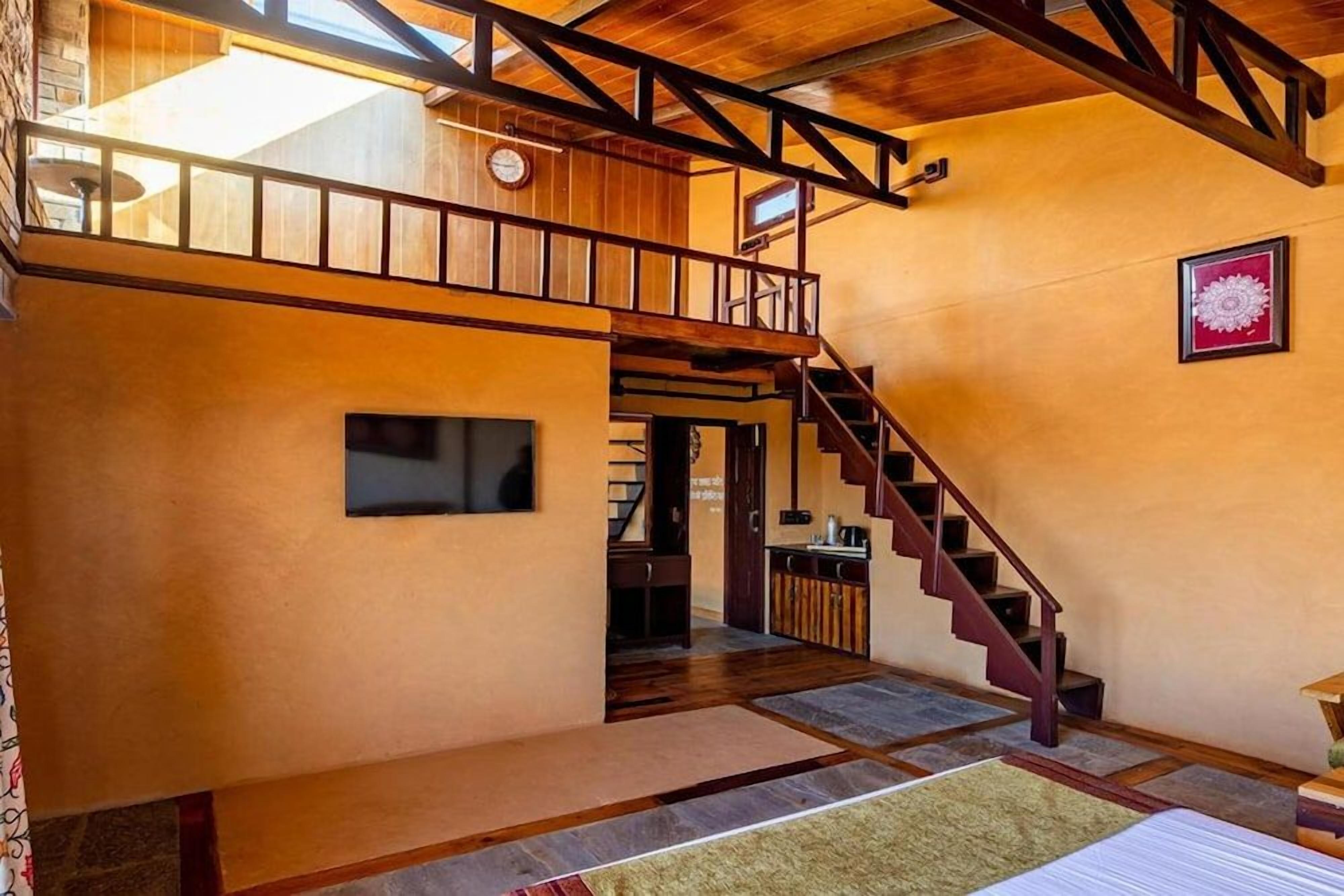 Um interior espaçoso com escada de madeira, um mezanino e uma grande janela que permite entrada de luz natural.