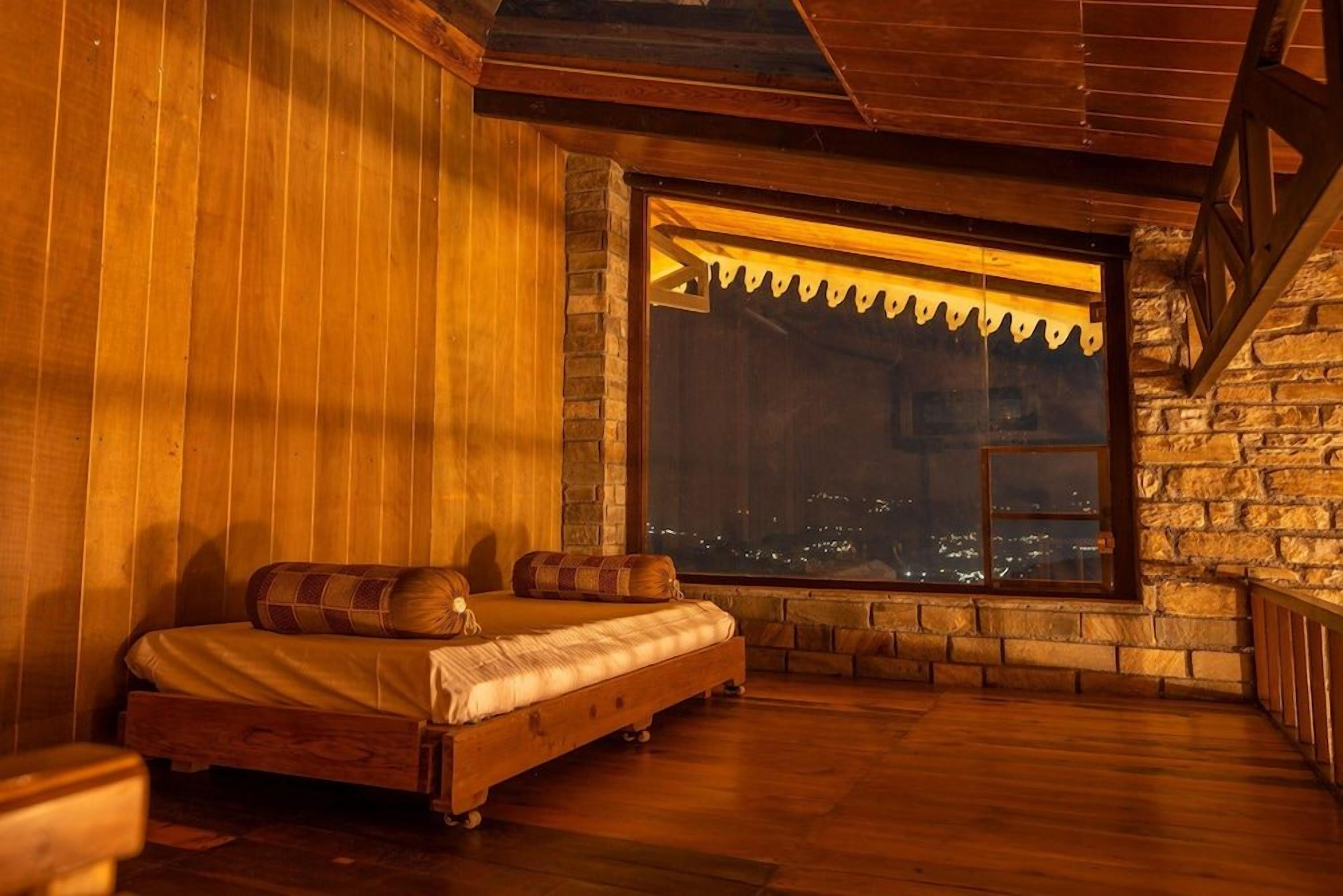 A cozy room with a bed, a window with a view of a cityscape, and wooden walls.