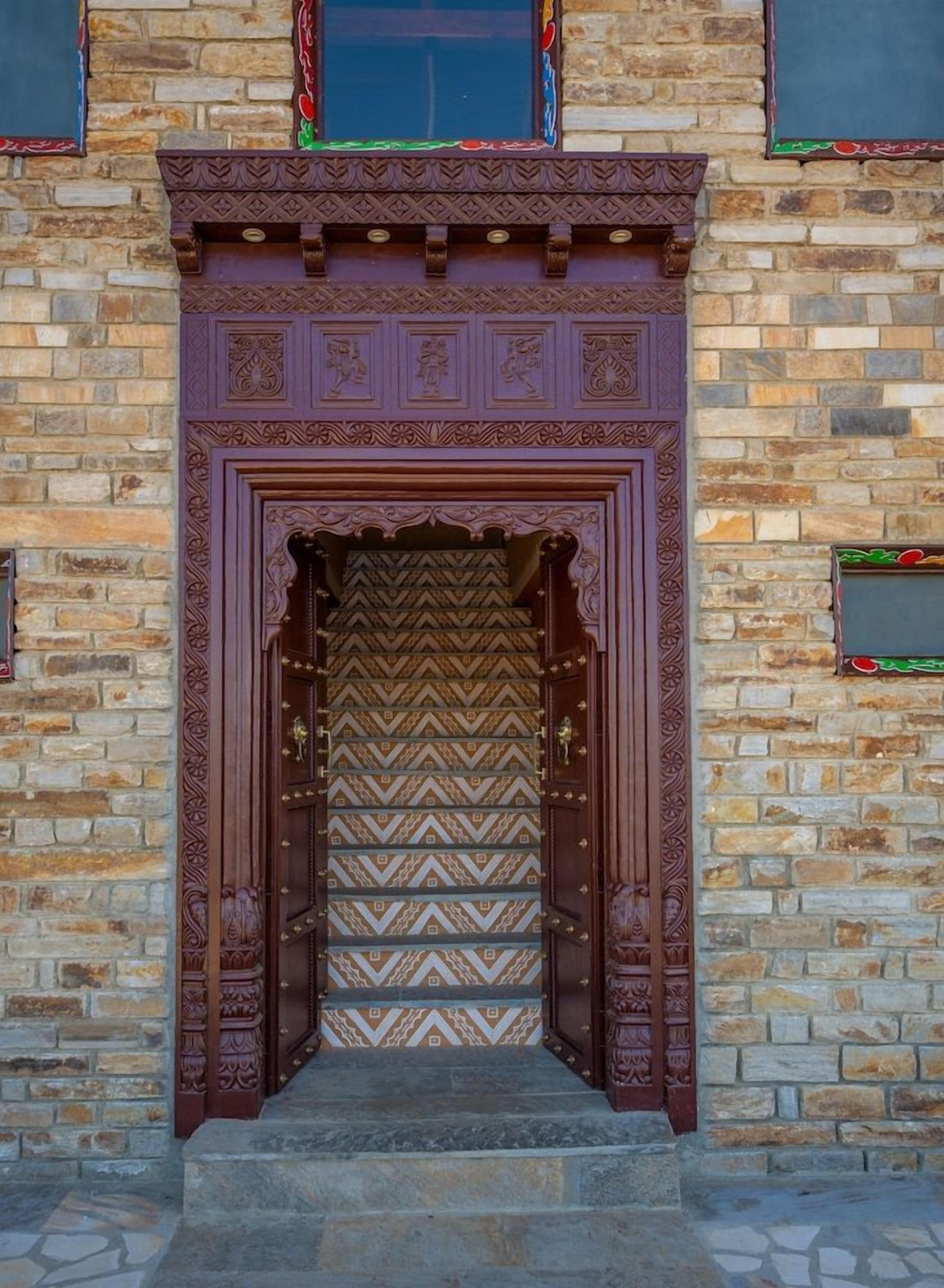 Una porta de fusta amb detalls escultòrics complexos i un disseny amb motius, encaixada en una paret de maó.