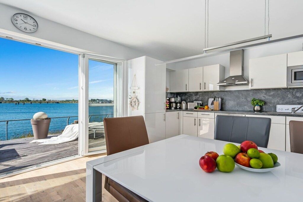 A modern kitchen with a view of a body of water, a dining area with a table and chairs, and a clock on the wall.