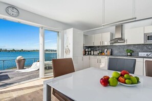 A modern kitchen with a view of a body of water, a dining area with a table and chairs, and a clock on the wall. - Holiday apartment with 2 bedrooms (Kappeln)