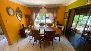 A dining area with a round table and chairs, a clock, and a window with curtains. - Charming 2-bedroom estate with fitness room in Woodland Hills Estate (Woodland Hills Estate, Bloemfontein)