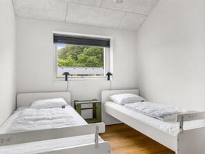 A room with two single beds, a window with blinds, a small table, and a view of trees and a building outside. - "Djuna" - 475m from the sea by Interhome (Haderslev)