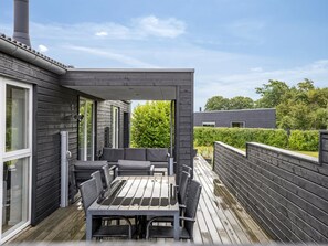 Un patio techado al aire libre con una mesa y sillas, una terraza de madera y vista a un edificio residencial.