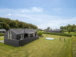 Una casa moderna con un patio trasero amplio, que incluye piscina y cancha de tenis.