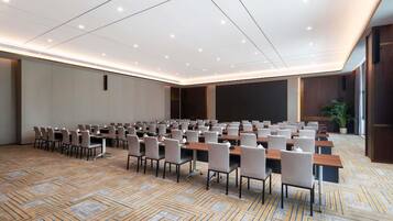 A conference room with rows of tables and chairs, a carpeted floor, and a large screen wall.