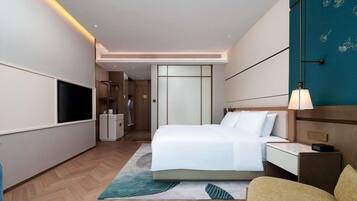 A modern hotel room with a large bed, bedside table, and a flat-screen TV.