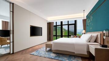 A modern hotel room with a large bed, a flat-screen TV, a desk, and a view of the outdoors.