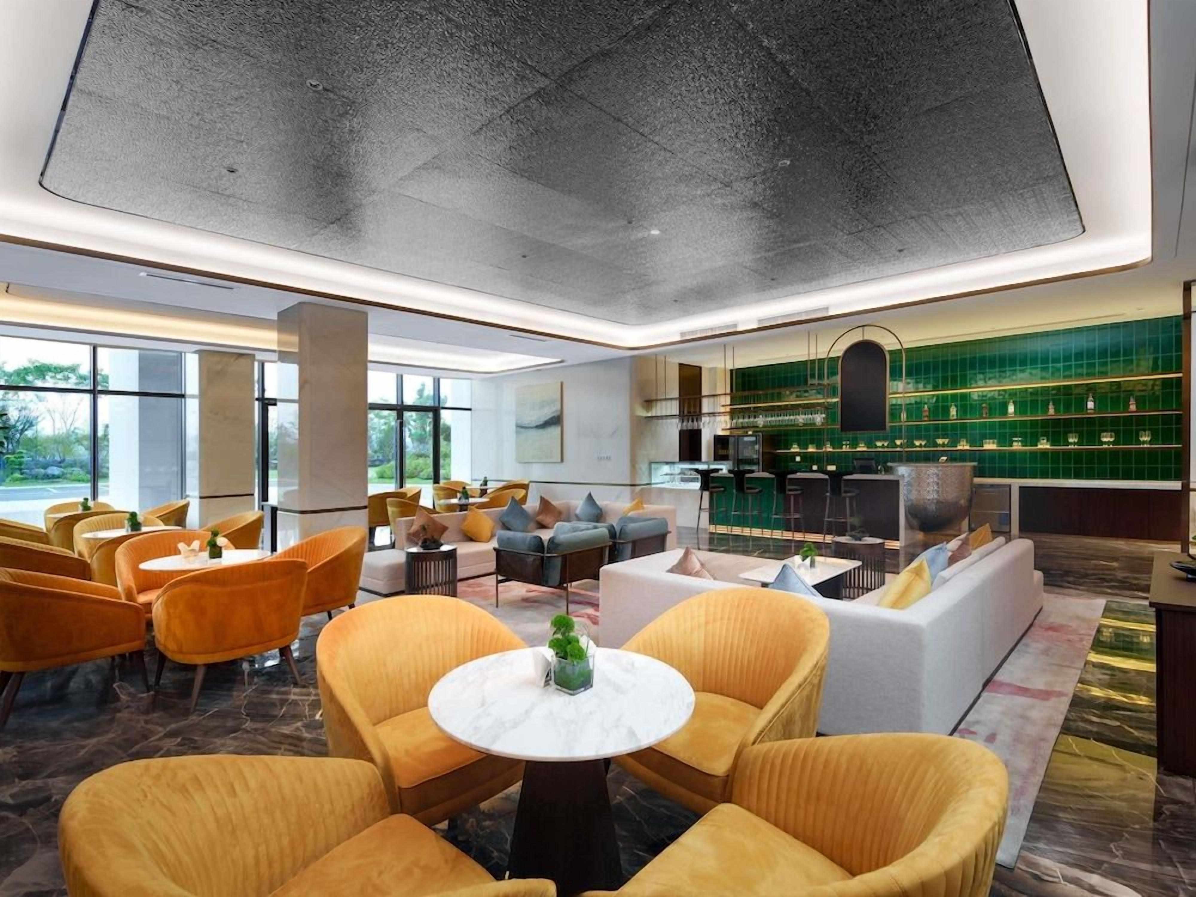A modern hotel lobby with seating areas, a bar, and large windows.