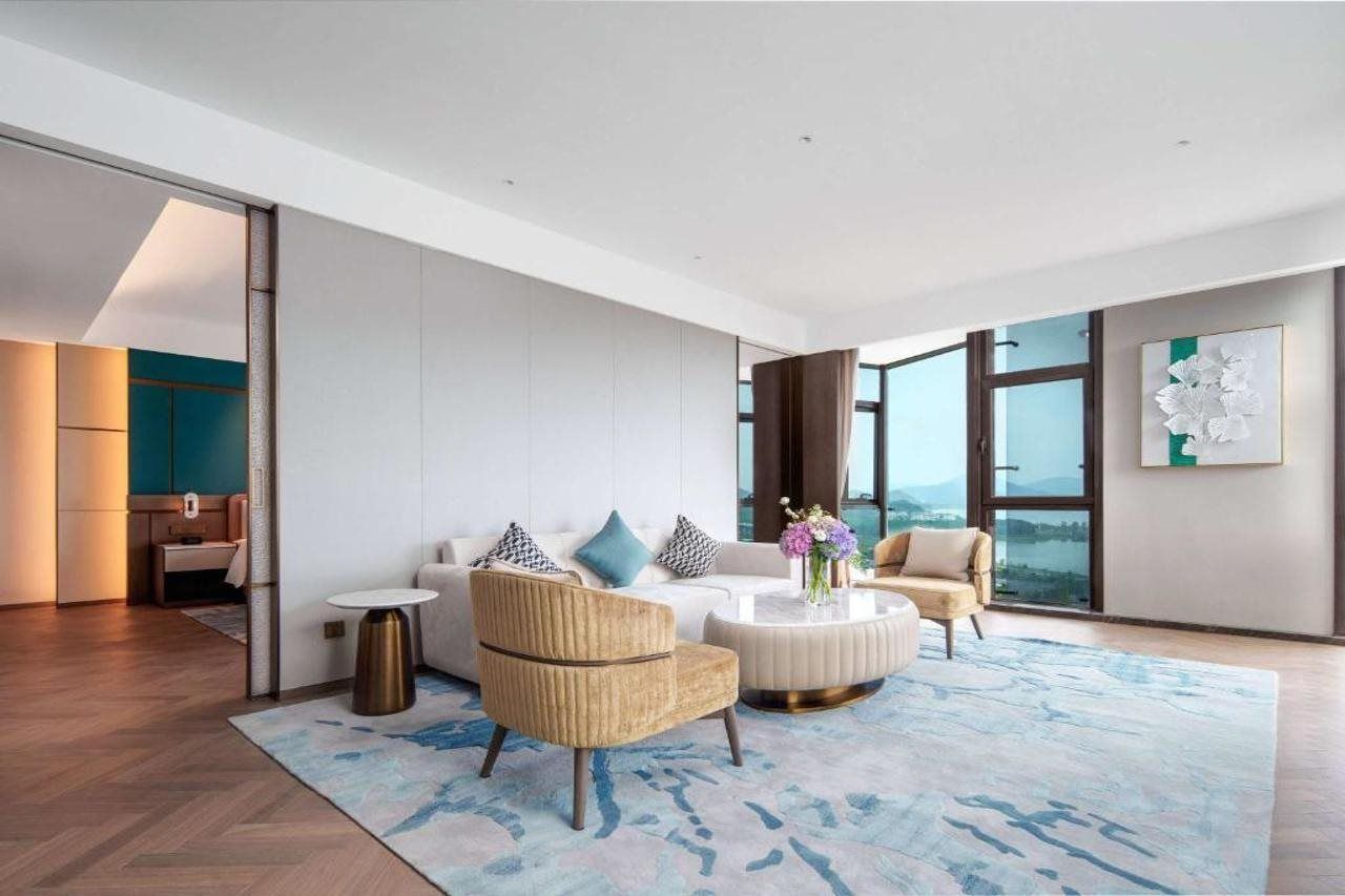 A modern living room with a sofa, armchairs, a coffee table, and a large window offering a view.