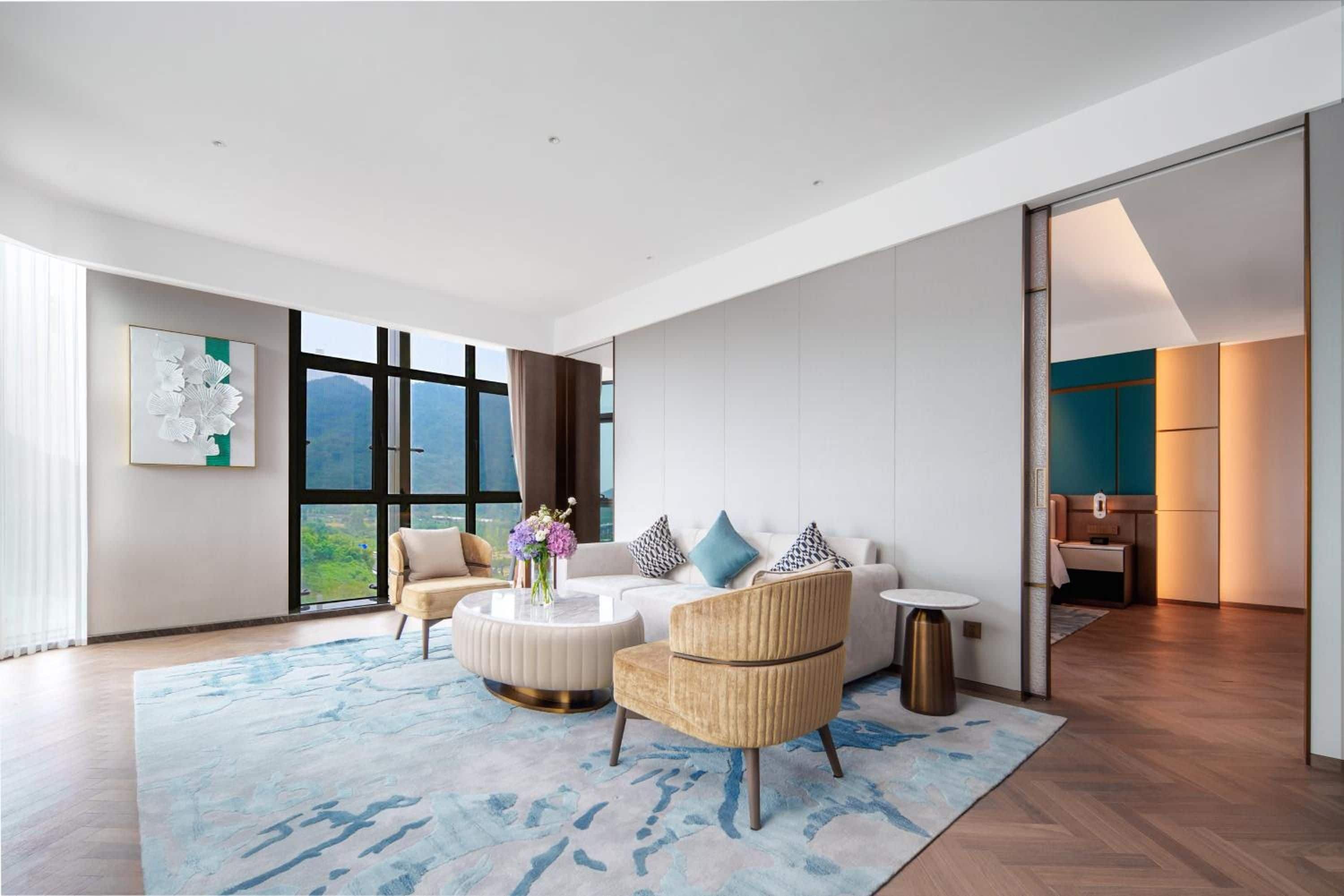 A modern living room with a sofa, armchairs, a coffee table, and a view of the outdoors through large windows.
