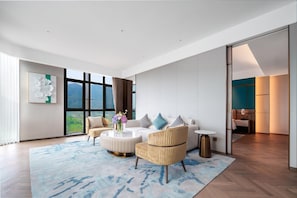 Una sala de estar moderna con un sofá, sillones, una mesa de centro y vistas al exterior a través de amplios ventanales.