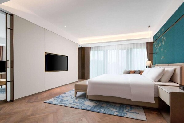 Een moderne hotelkamer met een groot bed, een flatscreen televisie aan de muur, een nachtkastje met een lamp en een groot raam met dunne gordijnen.