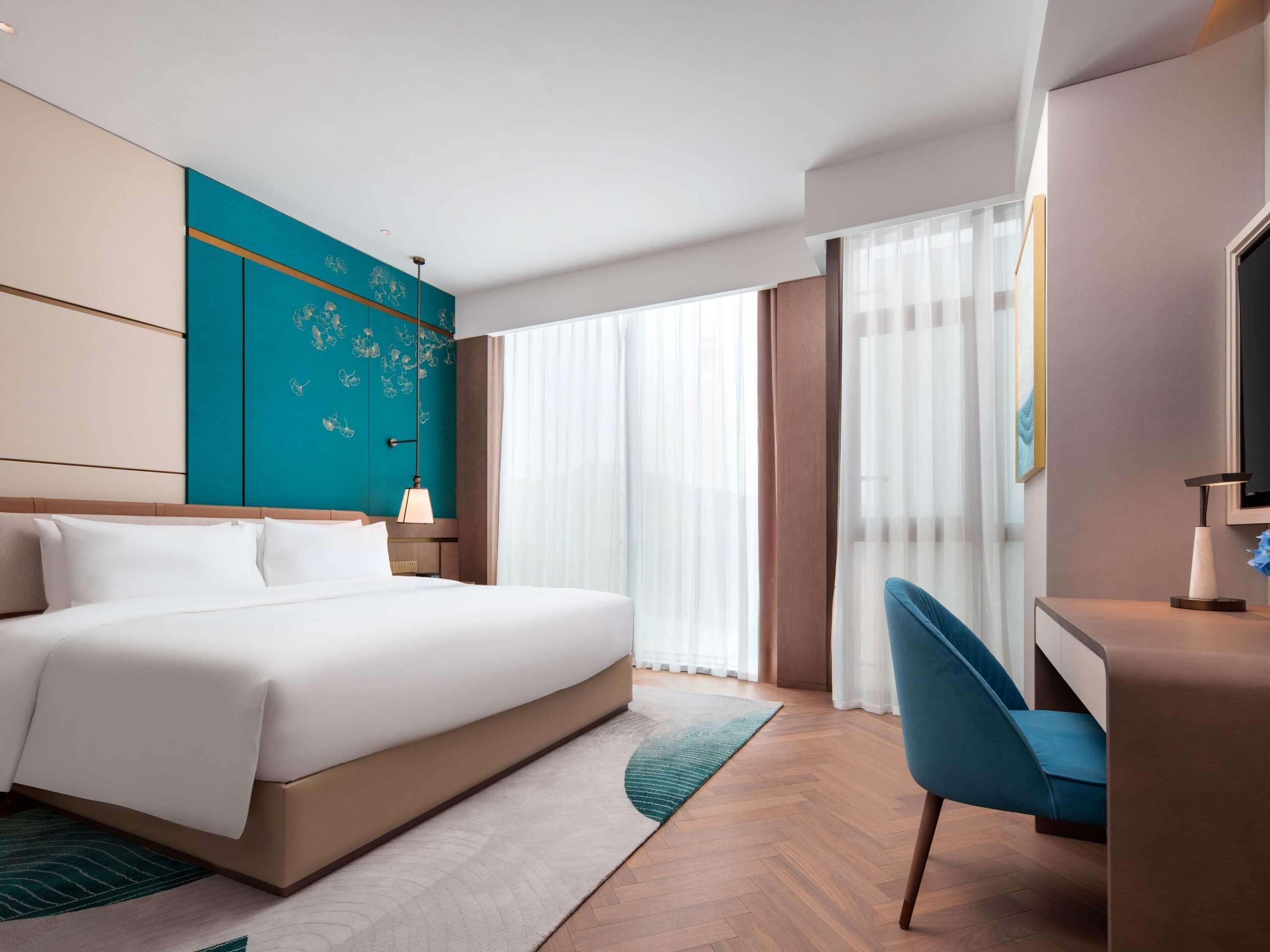 A hotel room with a large bed, a desk with a chair, a TV, and a window with curtains.