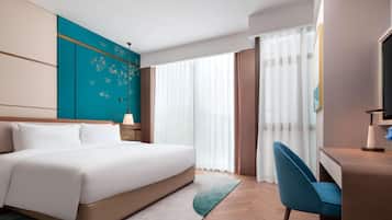 A hotel room with a large bed, a desk with a chair, a TV, and a window with curtains.