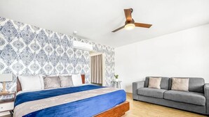 Un dormitorio con una cama, un sofá gris, un ventilador de techo y papel tapiz estampado.