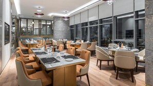 Un comedor moderno con varias mesas y sillas, ventanas amplias y lámparas de diseño contemporáneo.