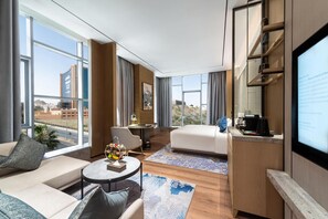 Habitación de hotel moderna con una cama grande, una zona de estar con una mesita de centro y una pantalla de televisión mostrando un mensaje.