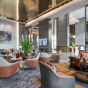 A modern lobby with seating areas, a large plant, and a television screen.