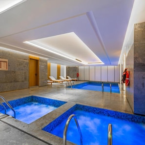 A modern indoor swimming pool with multiple lanes, lounge chairs, and a clear ceiling.