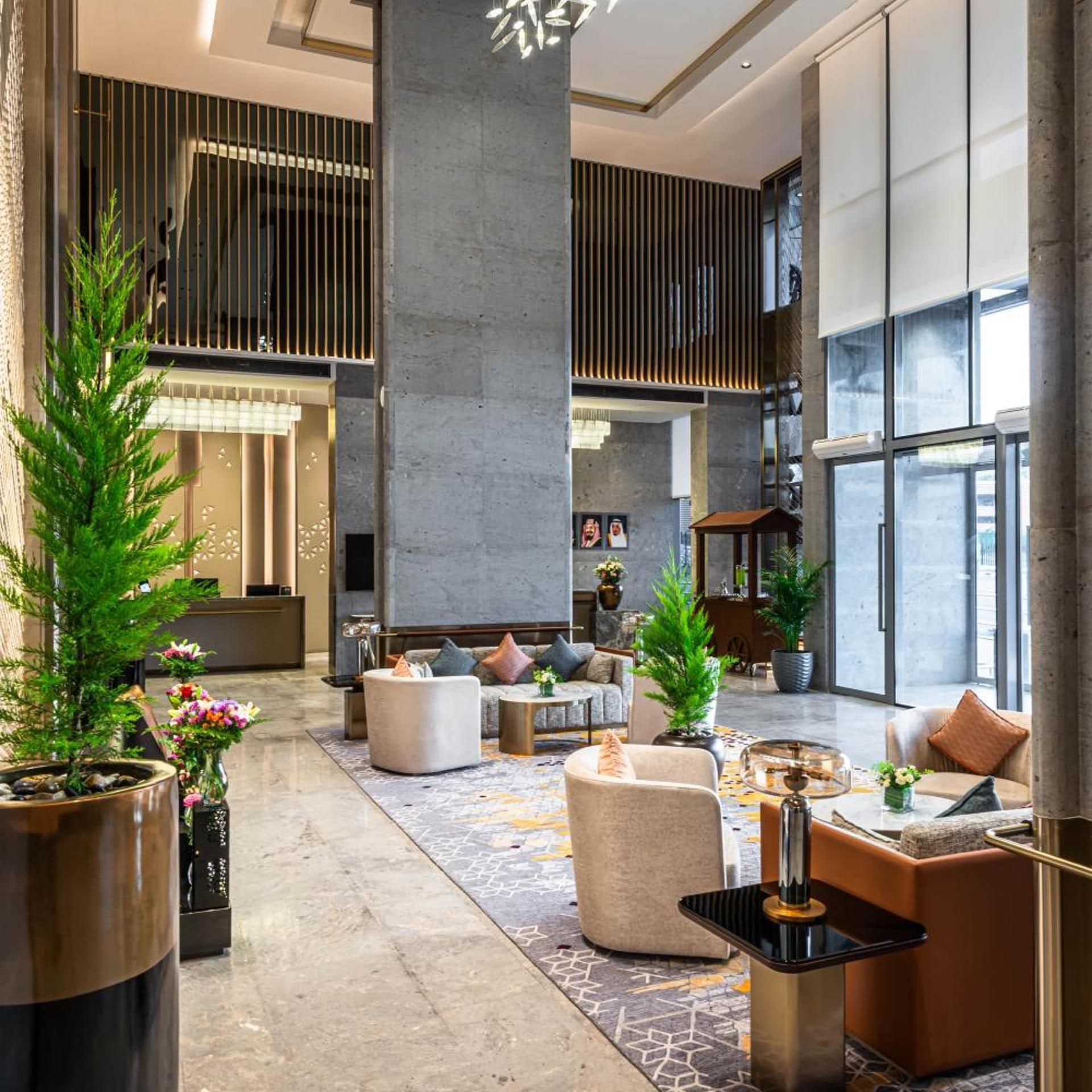 Un vestíbulo amplio con diseño moderno, que cuenta con una zona de estar central con sofás y sillones, un pilar grande y una variedad de plantas en macetas.