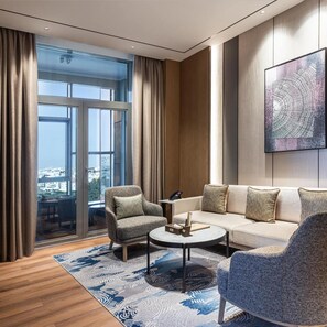 A modern living room with a sofa, two armchairs, a coffee table, and a large window with curtains.