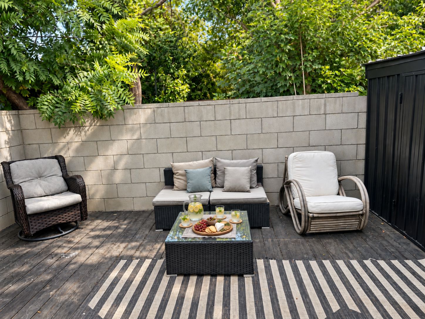 An outdoor patio with wicker furniture, a glass-top table, and a brick wall backdrop.