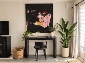 A living room with a black sofa, a black chair, a console table with a plant, a painting, and a television. - Secret Valley Guest House | Cozy & Private 1BR (Los Angeles)