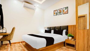 A hotel room with a bed, a desk, a chair, a nightstand, a potted plant, and a wall-mounted air conditioner. - Townhouse Oak Walmi Govindpur (Danapur)