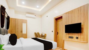 A modern hotel room with a bed, a TV mounted on the wall, a wooden wardrobe, and a small table with a chair. - Townhouse Oak Walmi Govindpur (Danapur)
