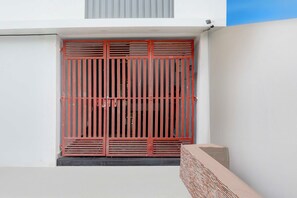 A red metal gate with vertical bars, a concrete step, and a white wall with a window above. - Townhouse Oak Walmi Govindpur (Danapur)