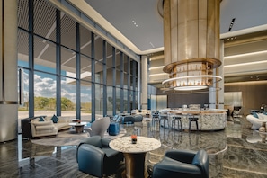 A spacious lobby with a marble floor, a central seating area with sofas and chairs, a bar with a circular marble countertop, and large windows offering a view of the outdoors. - Holiday Inn Kunshan East (Suzhou)