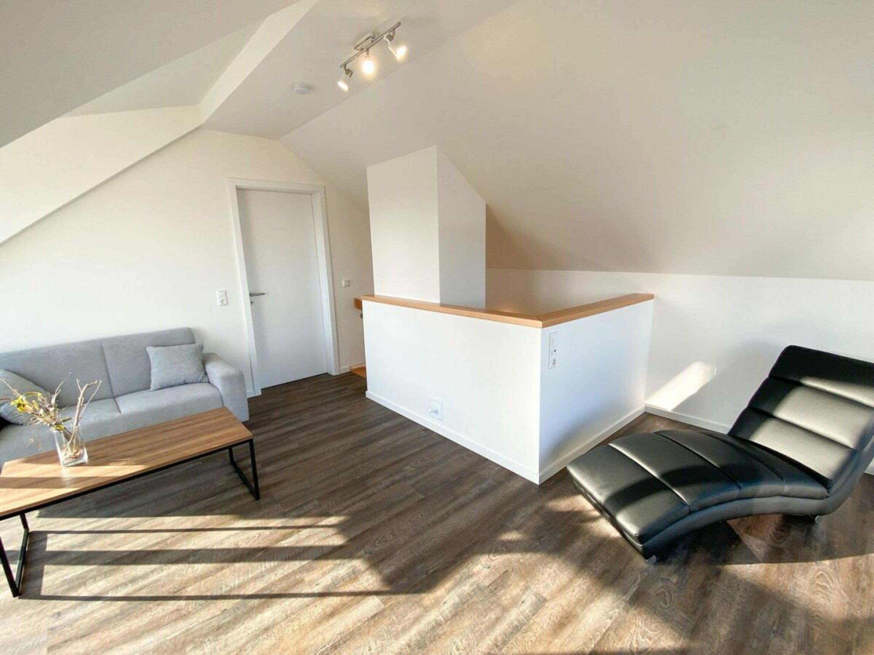 Ein moderner Wohnraum mit einer Loft-Decke, einem grauen Sofa, einem Holztisch, einem schwarzen Ledersessel und einem kleinen Schreibtisch.