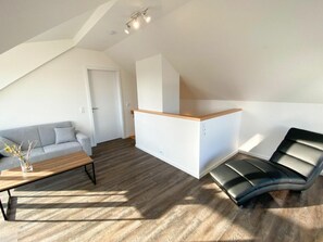 Ein moderner Wohnraum mit einer Loft-Decke, einem grauen Sofa, einem Holztisch, einem schwarzen Ledersessel und einem kleinen Schreibtisch.