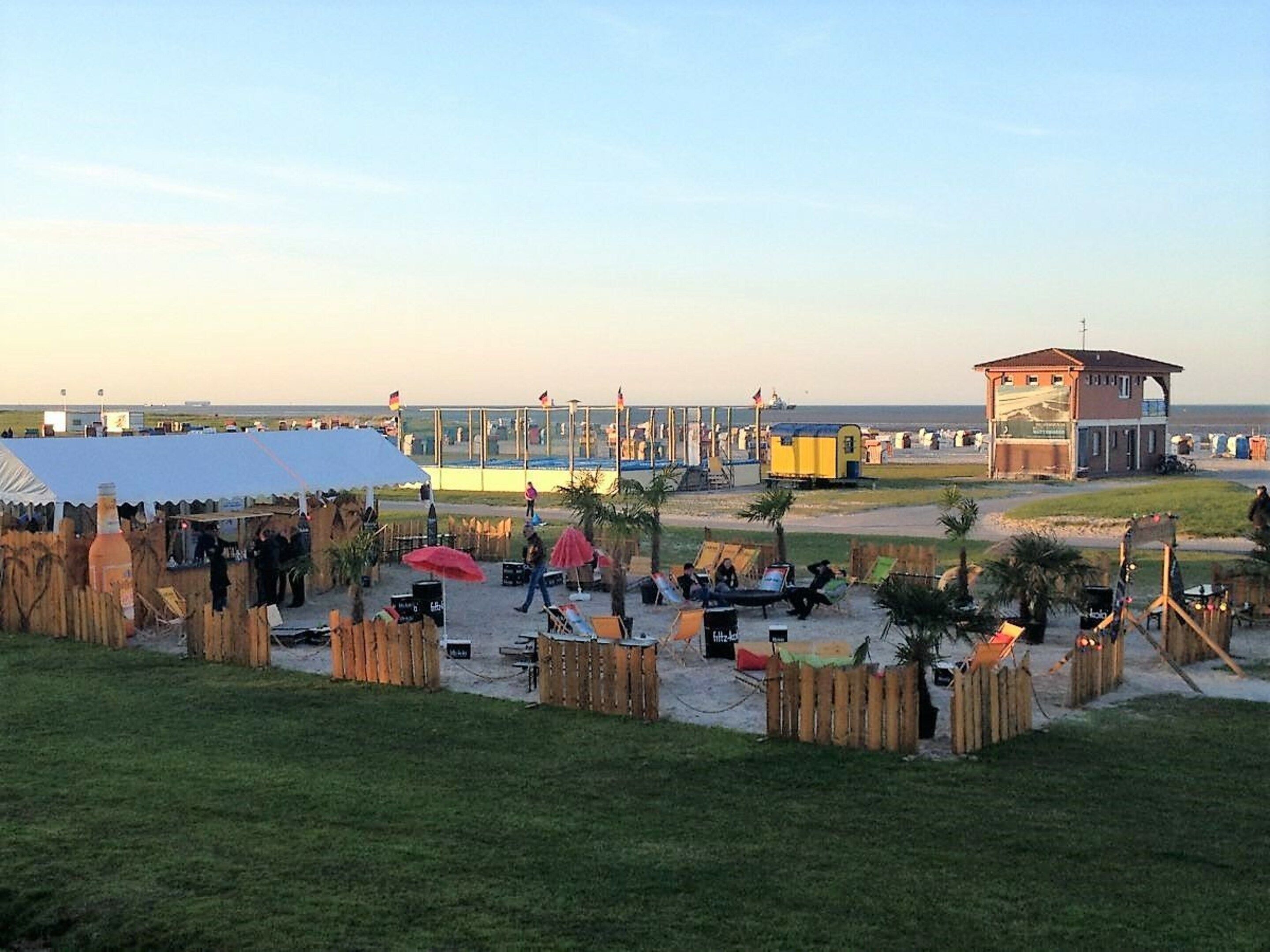 A beachside venue with a covered seating area, wooden fences, and a small building.