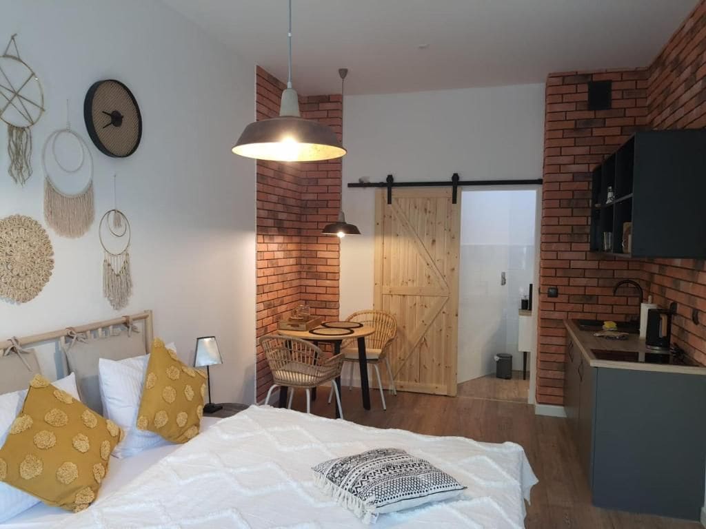 A room with a bed, a dining table, chairs, a hanging light fixture, a sliding barn door, and a kitchen area.