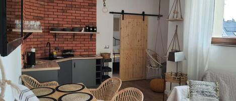 Una cocina acogedora con pared de ladrillo, armarios de madera y una zona de comedor con sillas de mimbre y una mesa.