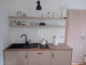 A kitchen with a black sink, wooden countertop, and white tiled backsplash. There are shelves above the sink holding jars and kitchenware.