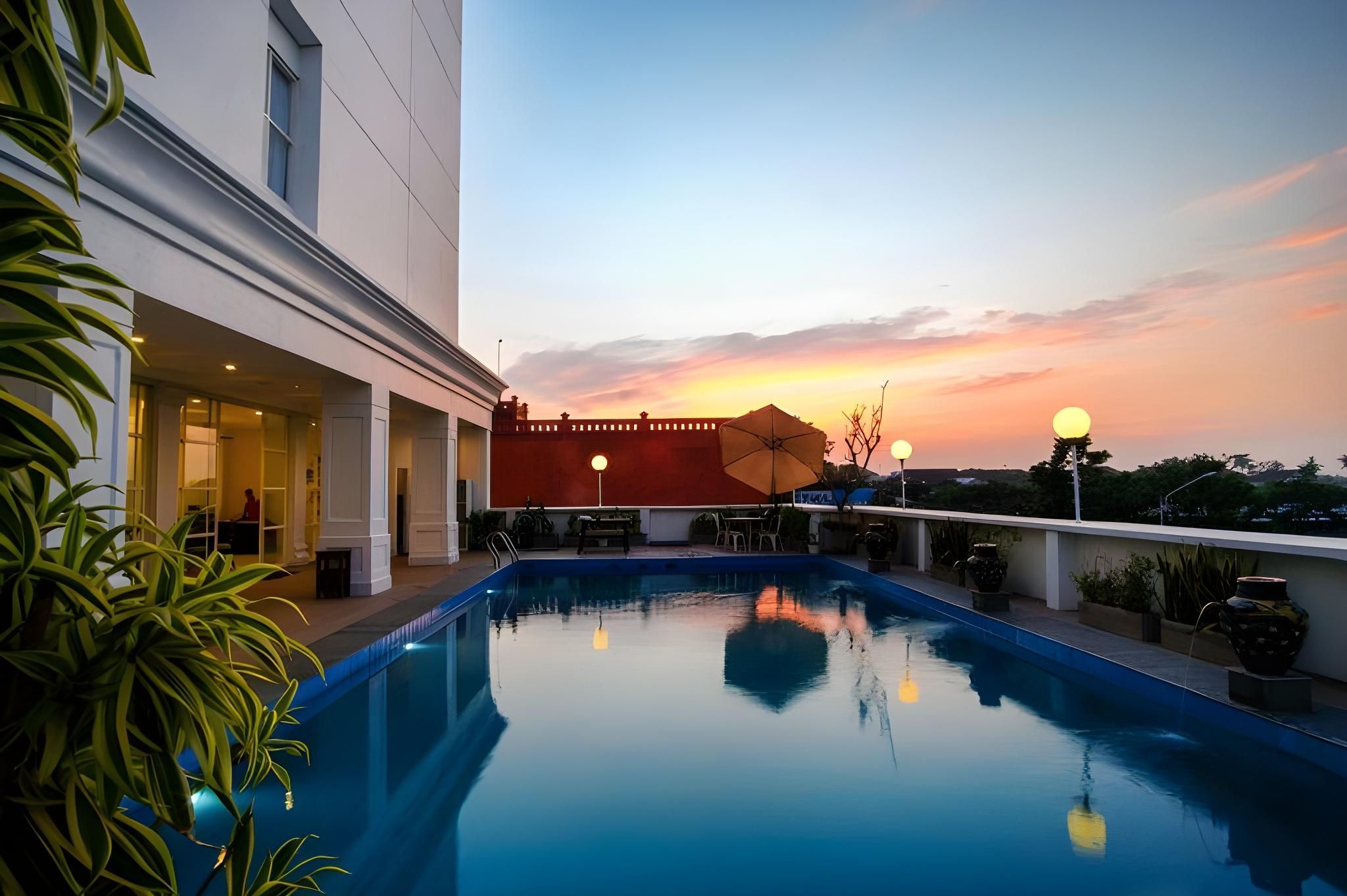 A swimming pool with a sunset view, a building with a red facade, and outdoor seating.