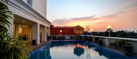 A swimming pool with a sunset view, a building with a red facade, and outdoor seating.