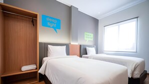 Una habitación de hotel con dos camas, un armario y una ventana.